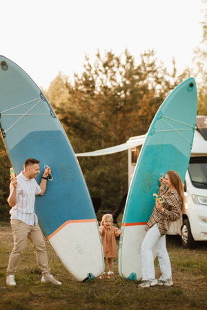 the family is resting next to their mobile home. Dad, mom and daughter play with sup boards and water pistols near a mobile home.の写真素材
