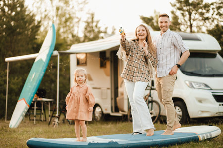 the family is resting next to their mobile home. Dad, mom and daughter play on sup boards with water pistols near the motorhome.の写真素材