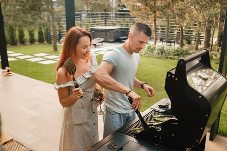 A married couple cooks grilled meat together on their terrace.の写真素材