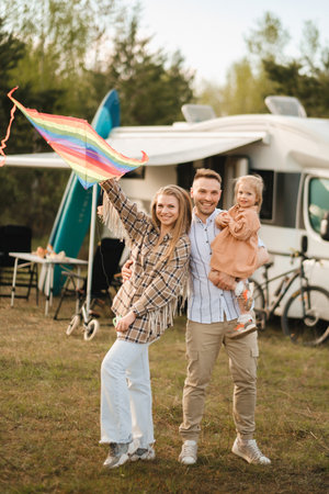Happy parents with their child play with a kite near their motorhome in the forest.の写真素材