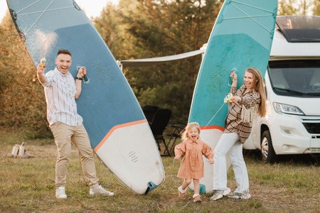 the family is resting next to their mobile home. Dad, mom and daughter play with sup boards and water pistols near a mobile home.の写真素材