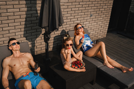 A happy family in swimsuits sunbathe in summer on their terrace on sun beds.の写真素材