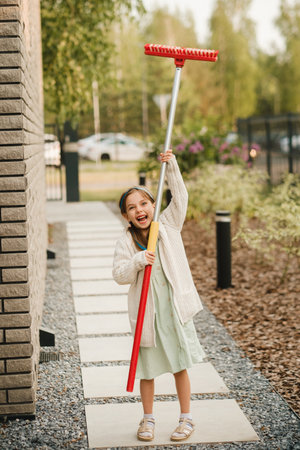 A little girl with a brush cleans a path on the street in the courtyard.の写真素材