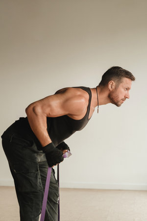 A man in black sportswear is engaged in strength fitness using a rubber loop indoors.の写真素材