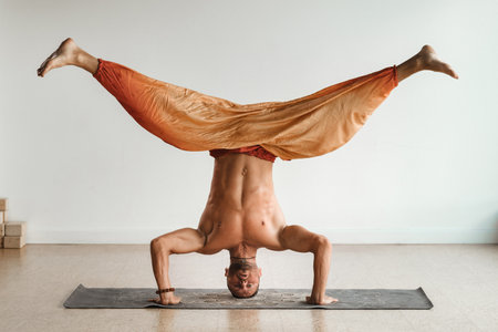 a man with a naked torso does yoga standing on his head indoors. Fitness Trainer.