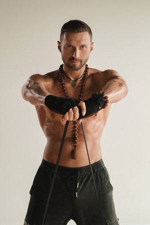 A man with a naked torso is engaged in strength fitness using a rubber loop indoors.の写真素材