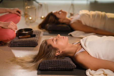 girls lying on the floor relax to the sounds of a Tibetan bowl in the fitness room.の写真素材