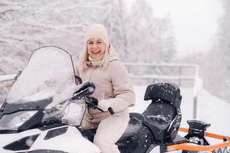 A cheerful woman rides a snowmobile in a winter forest.の写真素材