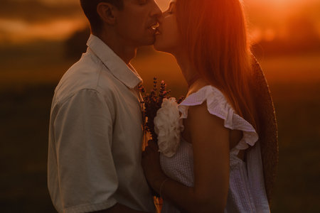 A couple in love in white clothes in a field at a red sunset.