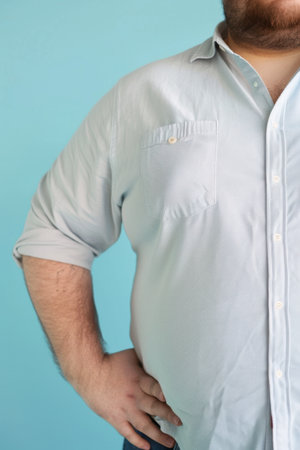The body of a fat man in a white shirt on a blue background. An overweight man in a white shirt.の素材