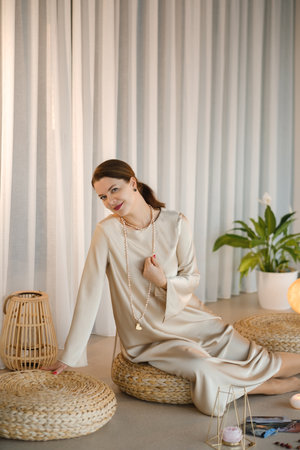 Beautiful Girl in beige dress and beads sitting indoors in front of practice.の写真素材