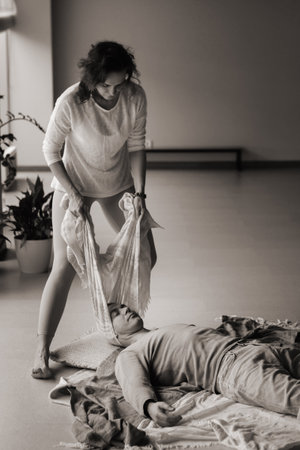 A therapist gently drapes a scarf over a person lying on a comfortable mat in a calm studio. The serene space is adorned with plants, creating a peaceful environment for healing and relaxation.の写真素材