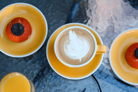 Warm latte art accompanied by two orange desserts on a sunny outdoor table setting during a relaxed afternoon brunchの写真素材