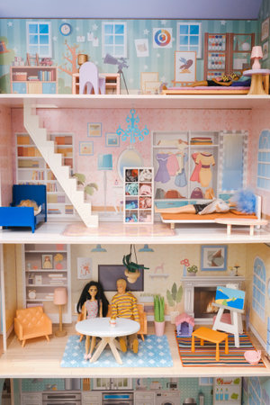 A vibrant dollhouse featuring multiple rooms filled with furniture and decorations. Two miniature figures are seated at a table, capturing a cozy domestic atmosphere.の写真素材