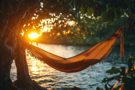 A bright red hammock hangs between rocks near the shore as the sun sets over a tranquil beach cove. The sandy area is framed by cliffs, creating a peaceful atmosphere perfect for unwinding.の素材