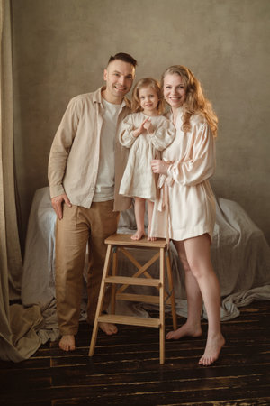 A joyful family stands together in their home, with a proud father and mother supporting their young daughter on a stool. Soft lighting enhances the warmth of the moment.の写真素材