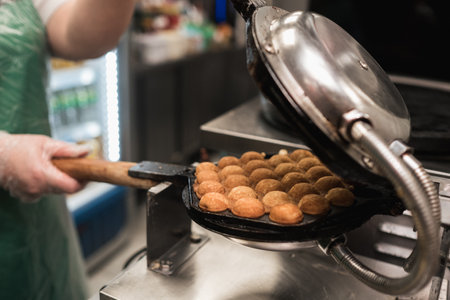A chef carefully prepares takoyaki using a specialized grill, turning the batter balls while surrounded by a bustling kitchen during the midday meal rush.の写真素材