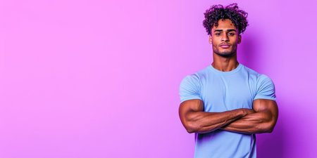 A young man poses with arms crossed, exuding confidence. He has a stylish hairdo and wears a light blue t-shirt. The bright purple backdrop emphasizes his athletic build and relaxed demeanor.の素材