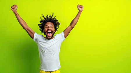 A young man with curly hair exuberantly raises his arms in celebration against a vibrant green background, showcasing pure joy and enthusiasm during a lively occasion.の素材