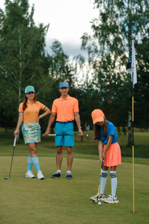 Family enjoys a fun day of golfing on a sunny afternoon at the course, with a youngster preparing to putt as parents watch and cheerの写真素材