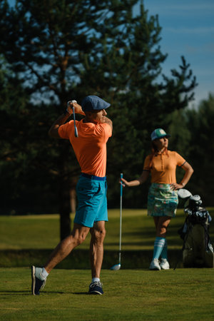 A man hits a ball on a golf course. A couple enjoys a sunny day playing golf on a bright green courseの写真素材