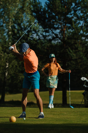 Golfers enjoying a sunny afternoon on a lush course, showcasing swings and style while preparing for a round of golf amidst tall treesの写真素材