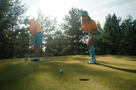 Golfers enjoying a sunny afternoon on a beautifully manicured course, celebrating a successful putt while surrounded by lush trees and greeneryの写真素材