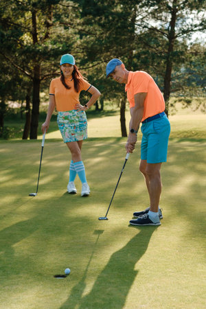 Couple enjoys a sunny afternoon playing golf on a lush green course while wearing vibrant, casual attire in a relaxed outdoor settingの写真素材