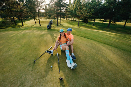 Couple enjoys a relaxing moment on the golf course in the late afternoon sun surrounded by lush greenery and golf equipmentの写真素材