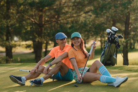 Portrait of a seated Couple on a golf course on a sunny day, showing relaxation and camaraderie while playing outdoor sportsの写真素材
