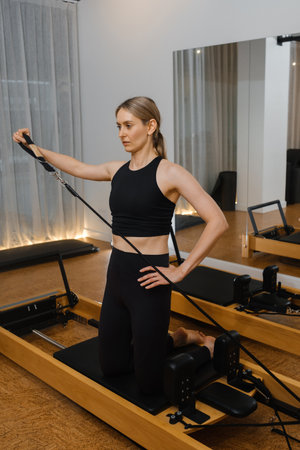 A woman engages in a pilates routine on a reformer, focusing on strength and posture in a bright and...