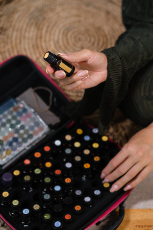A person is seen in a cozy home environment, holding a black essential oil bottle while exploring a vibrant collection of colorful bottles on a surface.の写真素材