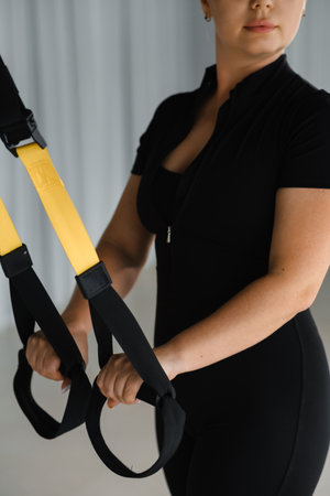 A woman engaged in suspension training holds yellow straps while focused on her workout in a well-lit fitness studio. The environment is designed for strength and flexibility training sessions.の写真素材