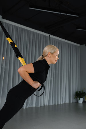 A woman focuses on her workout while performing a suspension exercise with resistance bands in a...