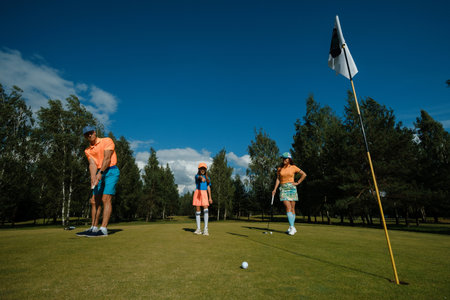 Family enjoying a sunny day of golf on the lush green course with clear skies and trees in the...