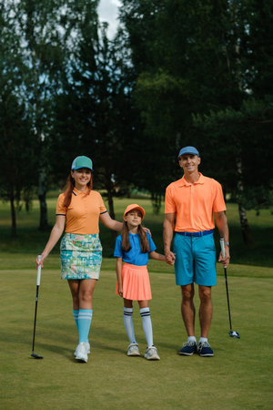 A cheerful family strolls hand in hand across a lush golf course. They wear vibrant colors, enjoying a sunny day filled with laughter and good times on the green.の写真素材