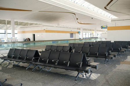 A large, open seating area in a contemporary airport terminal features rows of black chairs arranged...