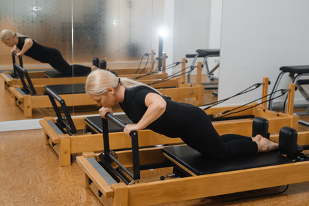 Woman practicing pilates on reformer equipment in a bright studio during a morning workout session...