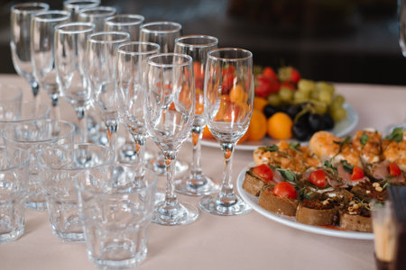 Elegant table setting for a celebratory event featuring a variety of drinks, fruits, and gourmet snacks on a neatly arranged surfaceの写真素材