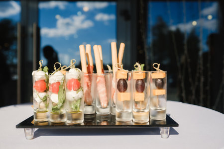 Unique appetizer display featuring elegant small glasses filled with fresh ingredients and flavors at a sunny outdoor event in the afternoonの写真素材