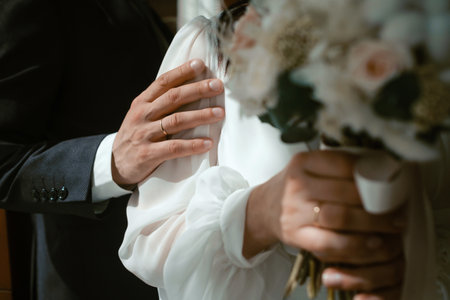 Couple sharing a romantic moment, showcasing wedding rings and bouquet in a soft-lit indoor setting...