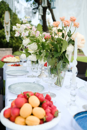 Elegant outdoor dining setup with vibrant flowers and fresh fruits in a serene garden during a sunny...