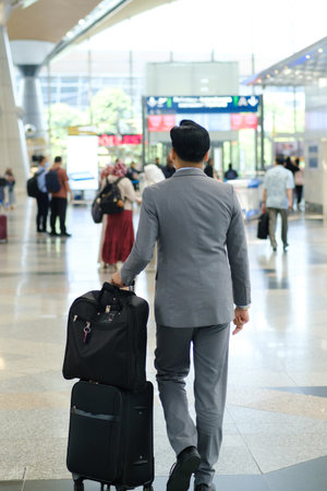 Business traveler in smart suit walking through bustling airport terminal with suitcase in tow during the dayの写真素材