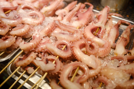 Freshly prepared octopus skewers served on ice at a seafood market in a vibrant coastal city during a bustling eveningの写真素材