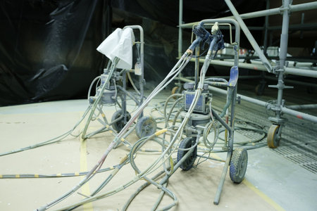 Two paint sprayers are set up at a construction site with hoses and equipment arranged around them. The area is prepared for painting, showing a focus on ongoing work.の写真素材