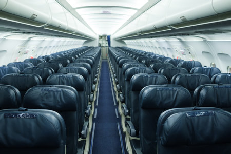 A spacious airplane cabin shows neatly arranged dark leather seats on either side of a central aisle. The area is empty, preparing for travelers before takeoff.の写真素材