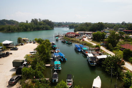 Merang Jetty Pier. Malaysia. July 25, 2025. Scenic view of Merang Jetty pier with moored boats and cars parked along the riverbank in a tropical location in sunny weatherのeditorial素材