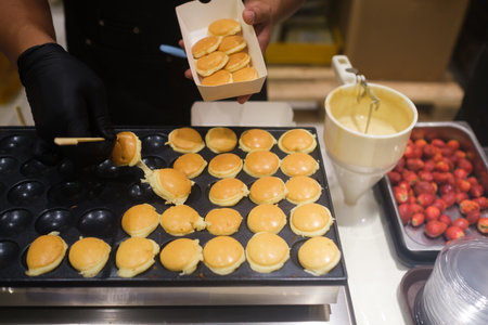 Baker prepares mini pancakes with strawberries in a lively kitchenの写真素材