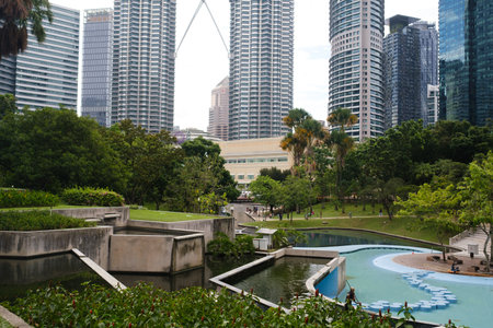 Kuala Lumpur. Malaysia. August 11, 2025. Stunning view of the fountain in the green city park. Wonderful urban landscape with tall buildingsのeditorial素材