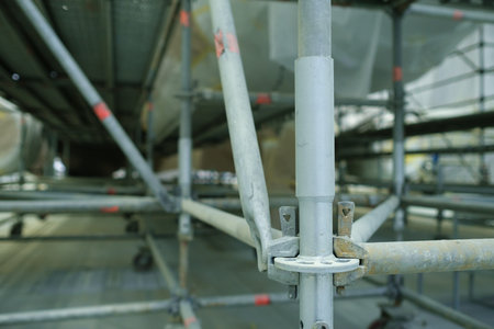 A large scaffolding system is set up inside a hangar, providing support for workers during maintenance on an aircraft. The scene shows metal frames and rolling wheels used for mobility.の写真素材
